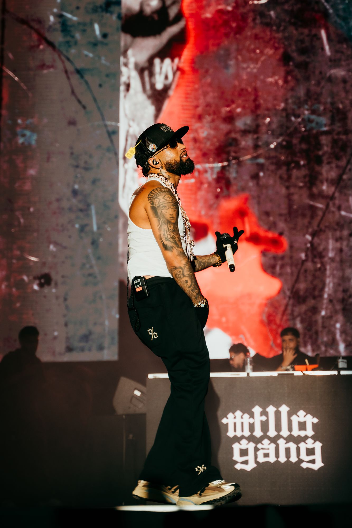 Bryant Myers crosses the stage at Roig Arena in Valencia wearing the black pants with the %, with the «millo gang» DJ booth behind him
